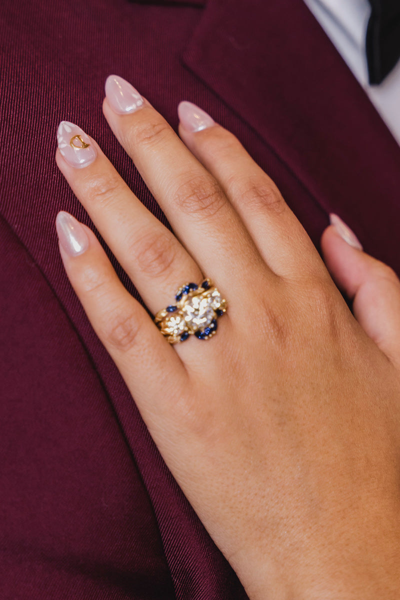Hand wearing a ring with a burgundy suit and white shirt in the background