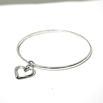 Silver bangle with a heart charm on a white background