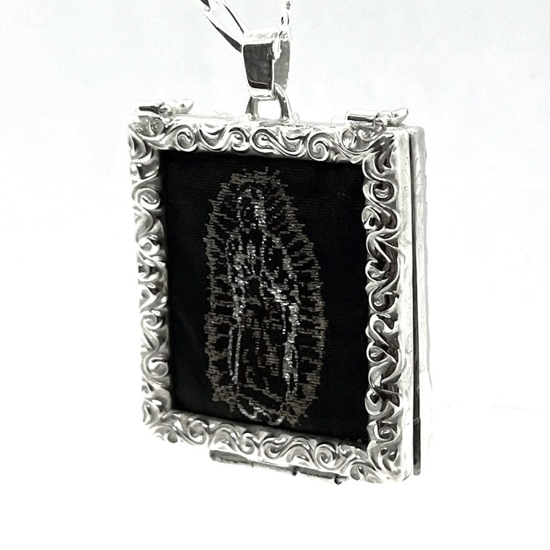 Silver-framed pendant with black fabric and embossed design on a white background