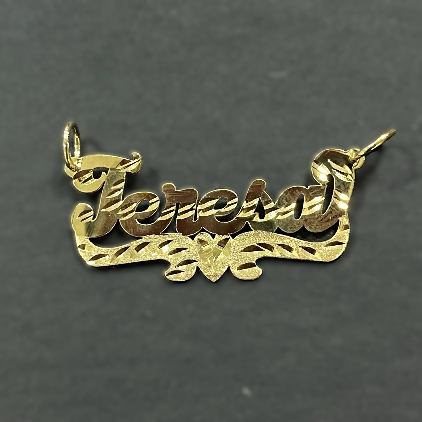 Gold name pendant with 'Teresa' on a dark gray background
